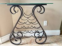 Front view of dark bronze metal wine rack side table with glass top