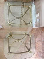 Pair of tables upside down showing glass tops, brass frames, rounded corners