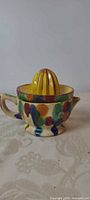 Side view of assembled two-piece pottery juicer showing handle, spout, multicolor glaze, yellow reamer