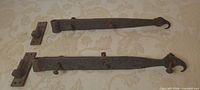Two strap hinges with hook finials and three eyes each, plus two pintle plates laid out on surface
