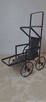 Side view of black metal doll carriage showing wheels, frame and seat