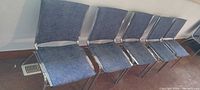 Five chrome frame blue fabric stacking chairs lined against wall
