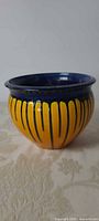 Front view of rounded ceramic planter showing yellow glaze with vertical blue drip detailing and blue rim