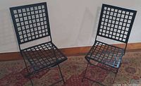 Two black wrought iron folding chairs displayed on rug against wall