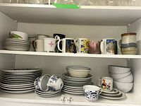 Upper cupboard shelves with assorted mugs, plates, bowls