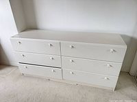 Front view of six-drawer white laminate dresser showing all drawers and knobs