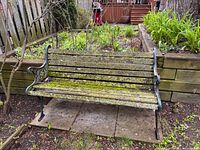Front view of entire bench showing moss-covered wood slats and cast metal ends