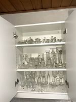Full view of three cabinet shelves loaded with assorted clear glass pieces