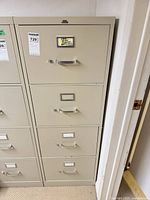 Front view of beige four-drawer metal file cabinet with handles and label holders