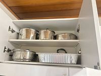 Cabinet shelves showing stainless steel pots with lids and aluminum foil roasting pan