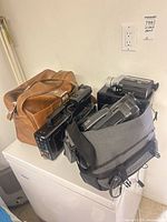Overview showing two Sony camcorders in grey bag, Nikon camera case, brown equipment bag and headphones