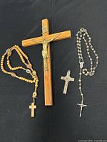 All four items laid out: wood wall crucifix, wood bead rosary, metal pendant crucifix, crystal bead rosary