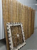Bamboo fencing roll standing against wall with framed metal scrollwork panel leaning in front
