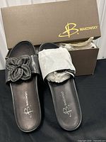 Top view of both slides showing flower embellishments and logo insoles beside branded box