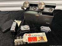 Group shot of all accessories including twin flash in case, Bauer flash, camera, light meter, flashbulbs, pouch