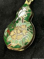 Front view of green cloisonné gourd locket with bird and flower design