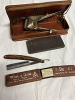Group layout of straight razor box opened, hair trimmer in leather case, sharpening stone