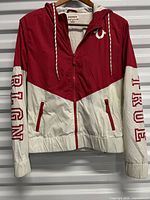 Front view showing color-block design, full zipper, drawstring hood, pockets, brand logo on chest