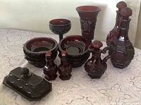 Full view of all ruby red Cape Cod pieces including decanter, cruet, vase, goblet, four bowls, salt and pepper, butter dish