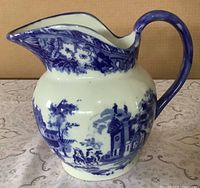 Side view showing spout, handle and village scene