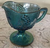 Side view of blue carnival glass footed creamer showing Harvest Grape pattern and iridescence