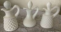 Front view of three milk glass cruets showing patterns and stoppers