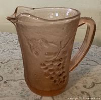 Side view showing pink glass pitcher, grape design, handle and spout
