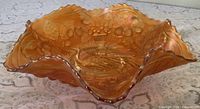 Oblique view showing iridescent marigold color, ruffled rim, interior peacock & urn design