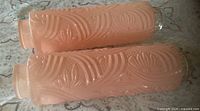Two pink cylindrical pressed glass lamp shades with floral relief pattern displayed side by side