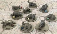 Group view of nine pewter cat figurines with breed labels and coloured balls visible