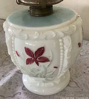 Close-up of milk glass base showing painted red flower and relief detailing