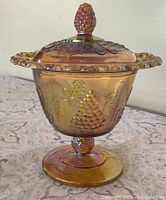 Side view of footed marigold carnival glass dish with lid showing grape relief