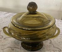 Front view of green glass lidded dish showing handles, pedestal base, and lid