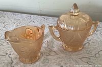 Front view of marigold carnival glass sugar bowl with lid and matching creamer