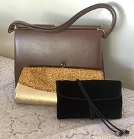 Front view of brown satchel with gold glitter clutch and black velvet clutch