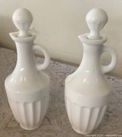 Front view of both milk glass cruets showing handles, stoppers, fluted bodies