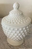 Front view of assembled white milk glass hobnail pedestal dish with lid