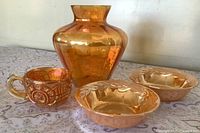Front view of all four glass items: two peach lustre bowls, amber carnival cup, orange iridescent vase