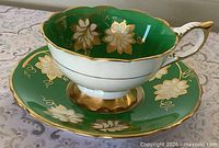Teacup and saucer showing green and gold leaf design and gilt details