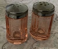 Front view of both pink depression glass shakers showing color, shape, and lids