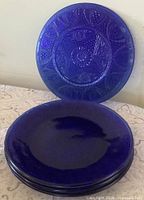 Stack of four sapphire blue pressed glass plates with pattern visible on top plate