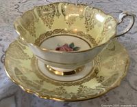Teacup on saucer showing pale yellow glaze, gold filigree, rose motif, gilt rims and handle