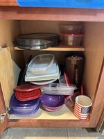 Cabinet shelf with stacked plastic containers, lids, purple colander, brown pitcher and flag mug visible