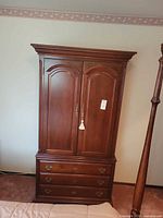 Front view of cherry veneer armoire showing doors, drawers, lock and tassel