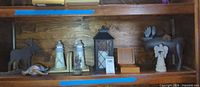 Shelf holding moose silhouette, lighthouse bookends, glass ship paperweight, metal lantern, jewelry box, angel figurine