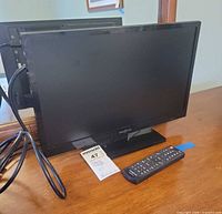 Front view of Insignia 19-inch TV on stand with remote and power cable visible