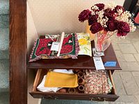 Overall view showing vase with faux roses, linens, candles, napkin rings inside drawer
