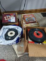 Two cartons and one tin filled with 45 RPM records, some in sleeves