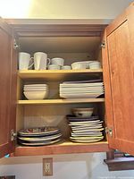 Cabinet view displaying mugs, bowls, square and rectangular white plates, patterned plates