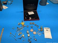 Overview of assorted jewelry pieces on blue background including necklace in Swarovski box, multiple earrings, rings, charms